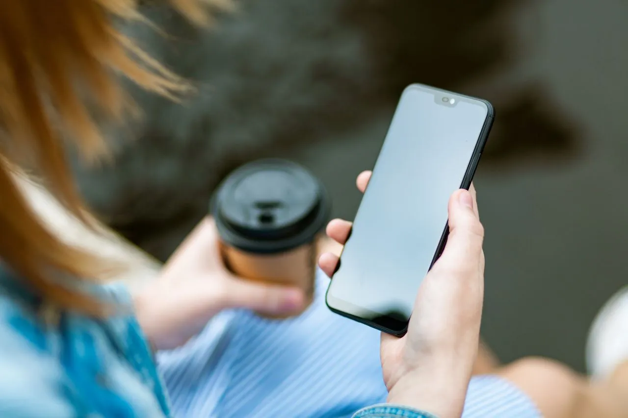 Person mit Smartphone und Kaffeebecher